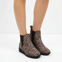 A pair of women's ankle boots with a brown and black leopard print pattern and black elastic side panels, shown on a model's feet against a white studio background.