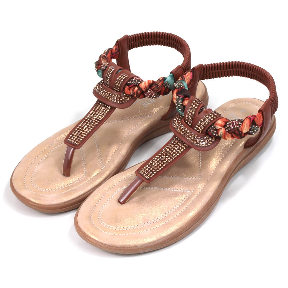 Tan coloured toe post sandals with elasticated back. Jewels and fabric decoration. Light tan coloured insoles. Angled view.