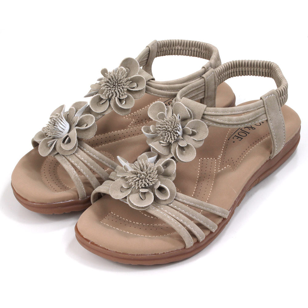 Suede look, light tan sandals with over toes straps and elasticated straps around the ankles. Suede look floral corsages over the feet. Tan coloured padded insoles. Angled view.