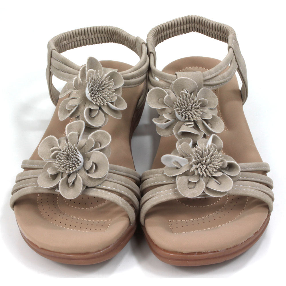 Suede look, light tan sandals with over toes straps and elasticated straps around the ankles. Suede look floral corsages over the feet. Tan coloured padded insoles. Front view.
