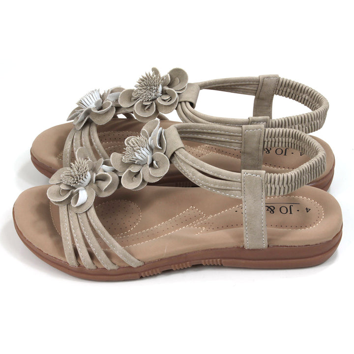 Suede look, light tan sandals with over toes straps and elasticated straps around the ankles. Suede look floral corsages over the feet. Tan coloured padded insoles. Side view.