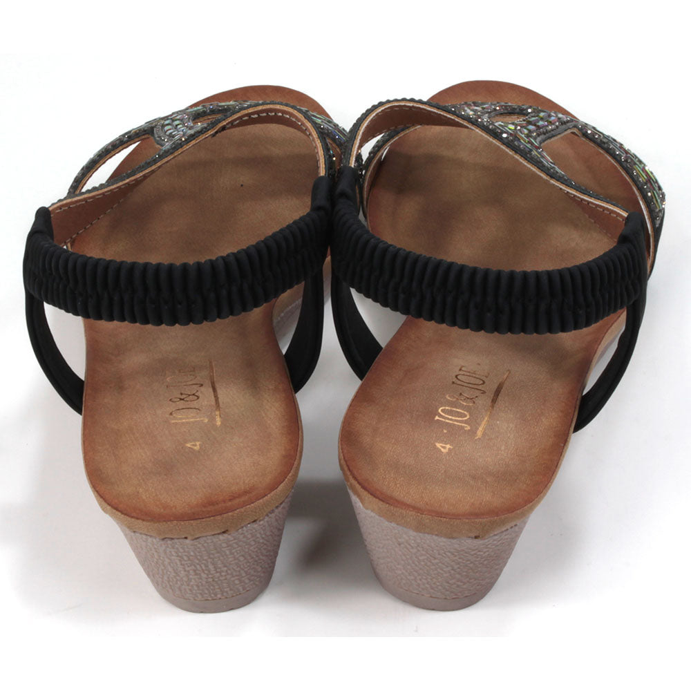 Sandals with black elasticated ankle straps. Over feet straps decorated with mosaics of sparkling jewels. Tan coloured insoles. Low heels. Back view.