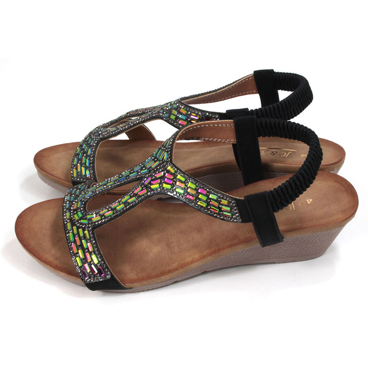 Sandals with black elasticated ankle straps. Over feet straps decorated with mosaics of sparkling jewels. Tan coloured insoles. Low heels. Side view.