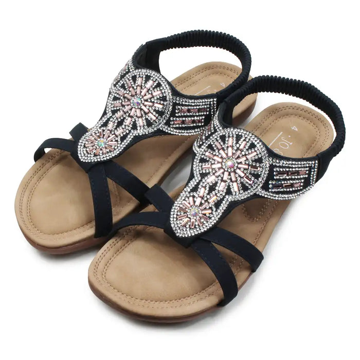 Beige sandals with black straps and decorative embellishments on a white background