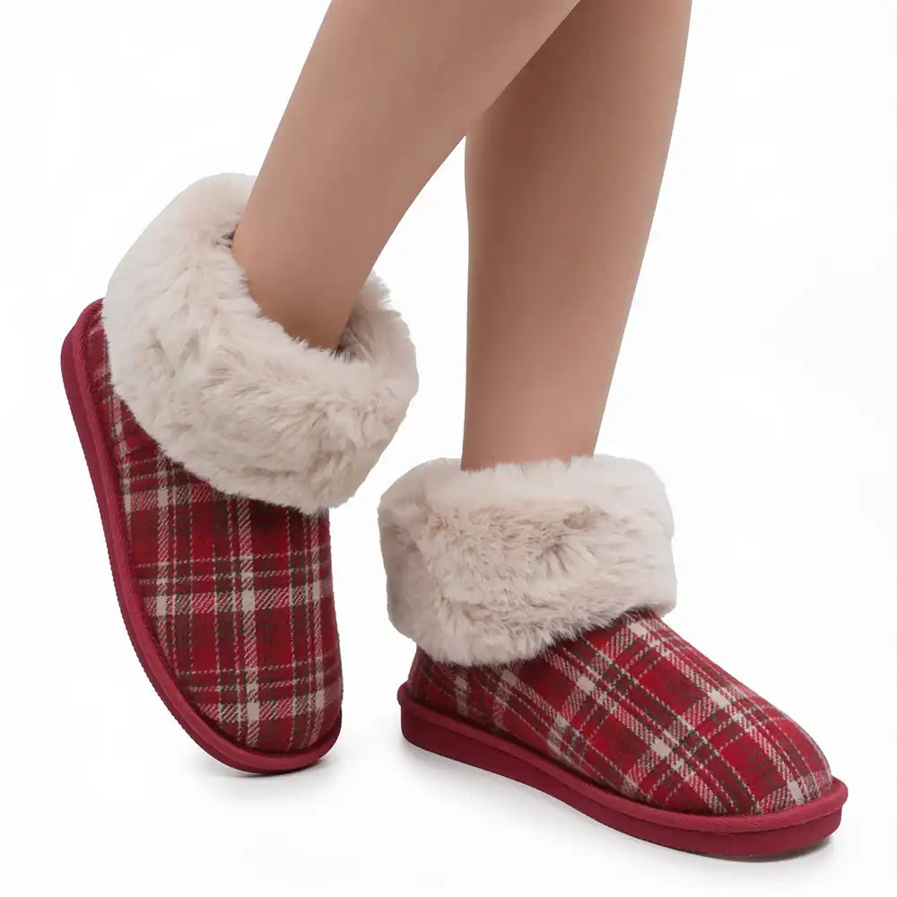 A pair of red and beige plaid slipper boots with thick cream faux-fur trim, shown on a model's feet against a white background.