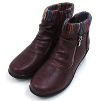 Burgundy ankle boots with knitted multicolour ankle cuffs. Zip fastening. Low  heels. Angled view.