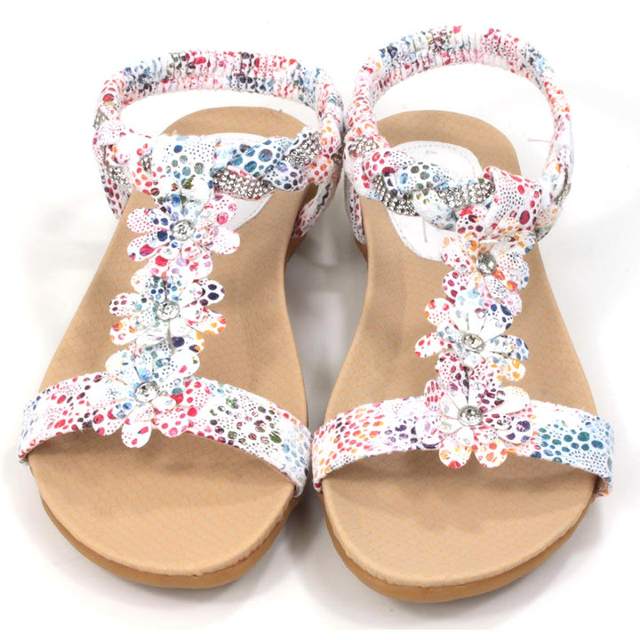Flat sandals with white straps decorated with multi coloured pattern. Floral detailing over the feet. Elasticated heel straps. Front view.