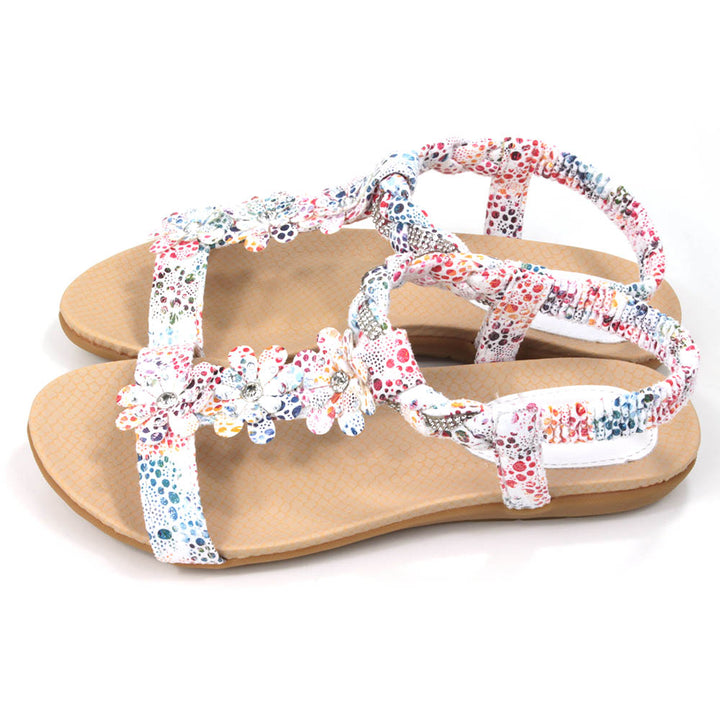 Flat sandals with white straps decorated with multi coloured pattern. Floral detailing over the feet. Elasticated heel straps. Side view.