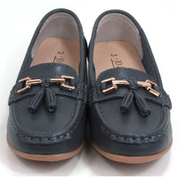 Joe and Jo moccasin style slip on, leather shoes in slate colour. Over the foot metallic gold coloured  detail and two matching tassels. Beige rubber soles. Front view.