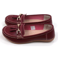 Joe and Jo moccasin style slip on, leather shoes in red wine colour. Over the foot metallic gold coloured  detail and two matching tassels. Beige rubber soles. Side view.