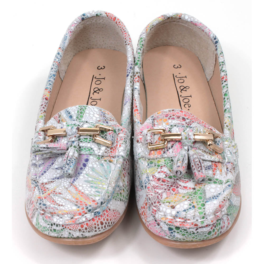 Jo and Joe Rio mocassin style slip on shoes. White background with floral mosaic style design. Gold bar and tassels details on foot. Front view