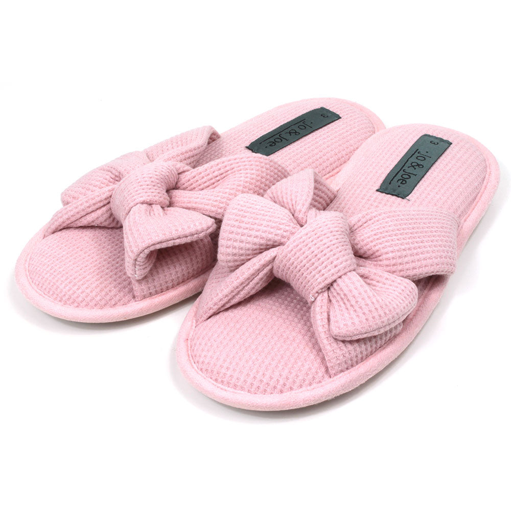 Pink slip on slippers with open toes and open backs. Pink waffle fabric. Padded footbed. Large bow over the foot. Angled view.