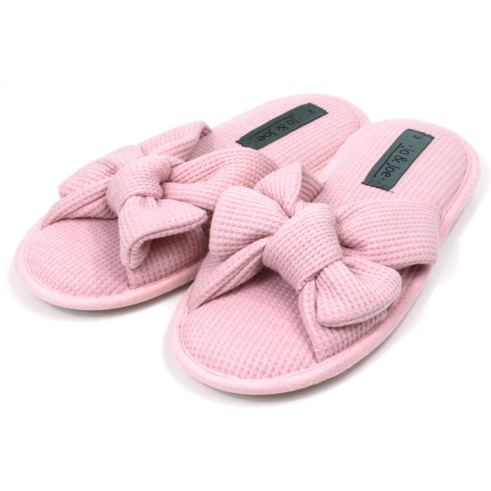 Jo and Joe pink slip on slippers with open toes and open backs. Pink waffle fabric. Padded footbed. Large bow over the foot. Angled view.