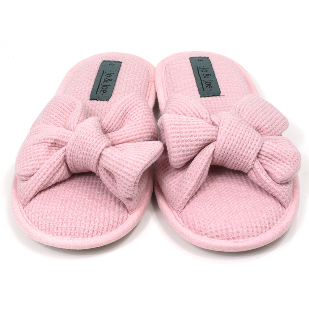 Pink slip on slippers with open toes and open backs. Pink waffle fabric. Padded footbed. Large bow over the foot. Front view.