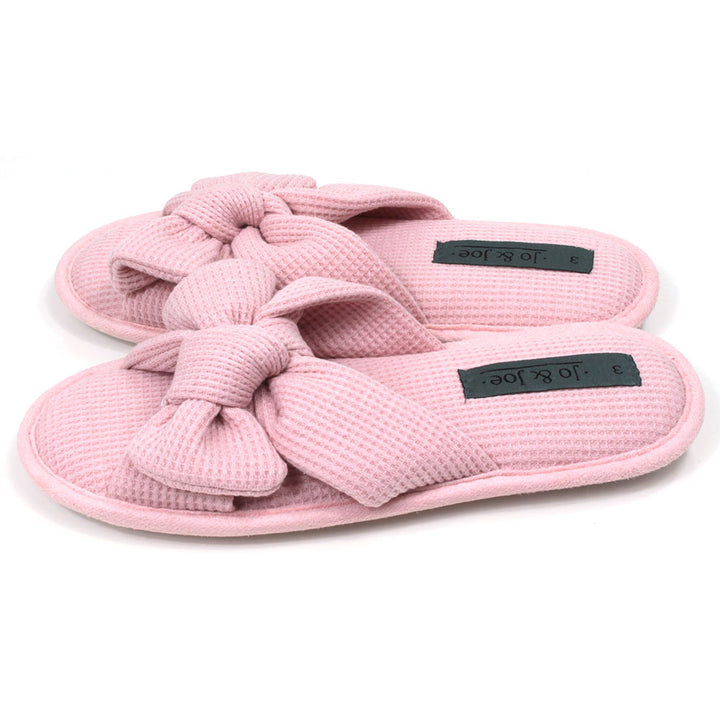 Pink slip on slippers with open toes and open backs. Pink waffle fabric. Padded footbed. Large bow over the foot. Side view.