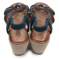 A pair of women's wedge sandals shown from the back, featuring navy blue elastic straps, braided woven straps with small red and white bead accents, a brown leather footbed, and a beige jute-wrapped wedge heel.
