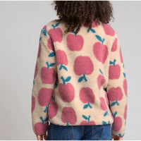 A person shown from the back wearing a cream sherpa fleece jacket with a pink apple pattern and blue leaf accents, paired with blue jeans, against a light gray studio background.