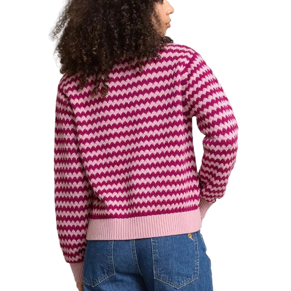 A person shown from the back wearing a pink and white chevron-patterned knit sweater with light pink ribbed trim, paired with blue jeans, against a plain studio background.