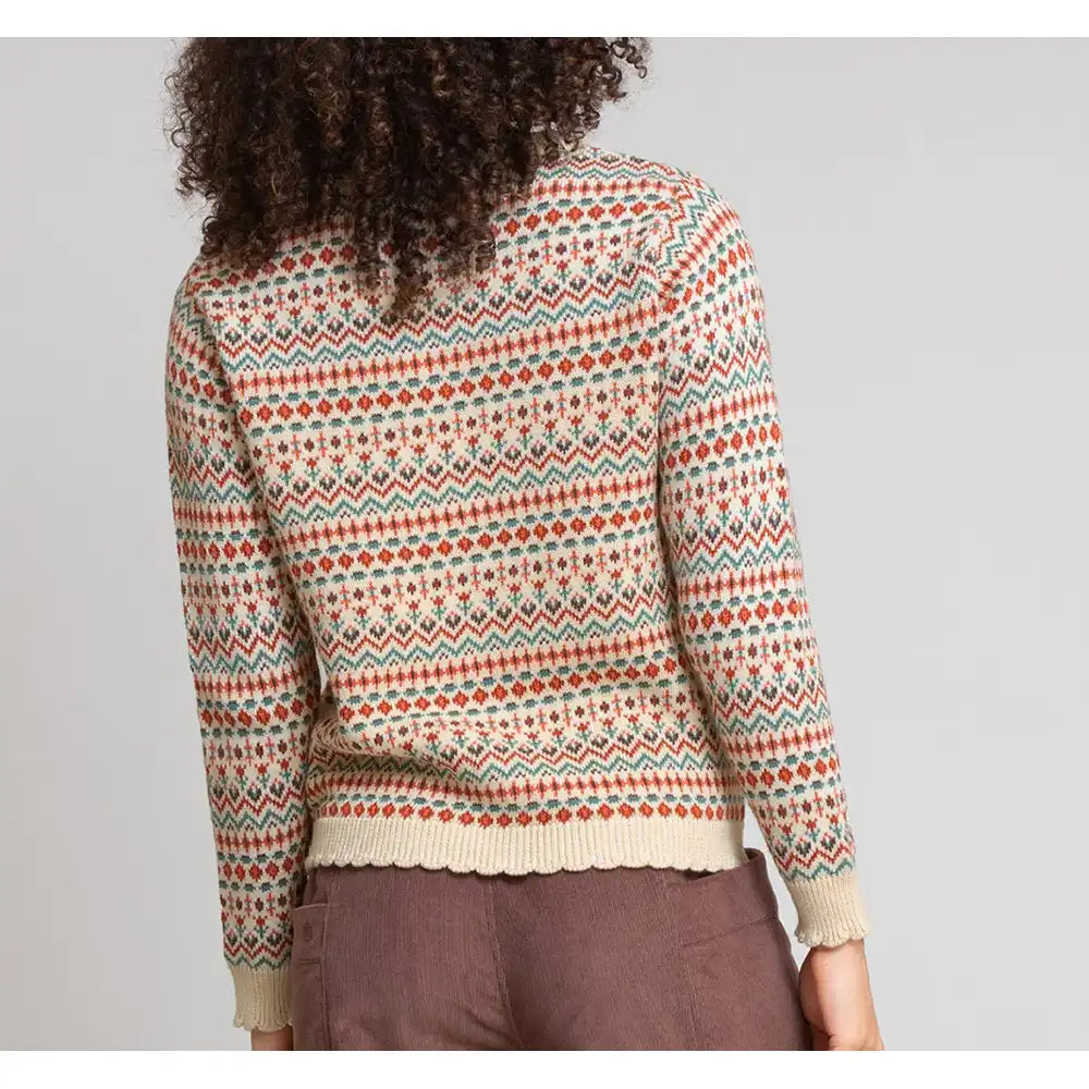 A person shown from the back wearing a long-sleeve knit sweater with a multicolor Fair Isle pattern in cream, rust orange, and teal, paired with brown trousers, against a light gray studio background.