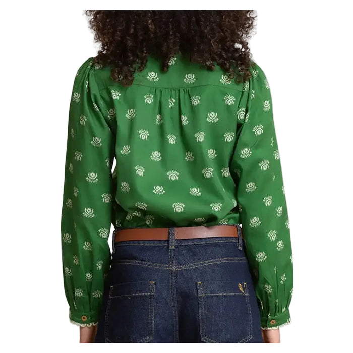 A woman shown from the back wearing a green long-sleeve blouse with a small white floral or leaf-like allover print, paired with dark blue jeans and a brown belt.