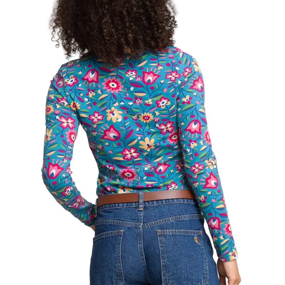 A woman shown from the back wearing a fitted long-sleeve top with a dense floral and botanical print in bright teal, pink, yellow, and green. 