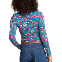 A woman shown from the back wearing a fitted long-sleeve top with a dense floral and botanical print in bright teal, pink, yellow, and green. 