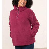 A woman wearing a dusty rose pink sherpa fleece quarter-zip pullover sweater with a mock neck and side pockets, paired with dark blue jeans, against a plain off-white wall.