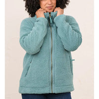 A woman wearing a teal sherpa fleece zip-up jacket, holding the collar closed. The jacket features a textured cable-knit pattern on the sleeves, a full front zipper, and side pockets, shown against a plain light beige background.