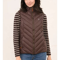 A woman wearing a brown puffer vest over a brown and cream striped long-sleeve shirt, paired with blue jeans, against a plain light background.