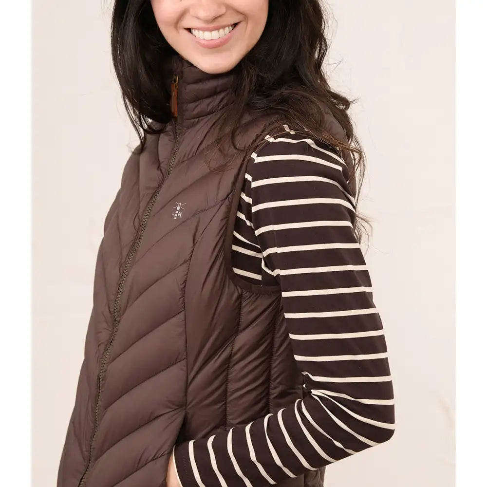 A woman wearing a dark brown puffer vest over a brown and cream striped long-sleeve shirt, shown from the chest up against a plain light background.