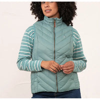 A woman wearing a sage green quilted puffer vest over a matching sage green and white striped long-sleeve top, paired with dark blue jeans, against a plain white studio background.
