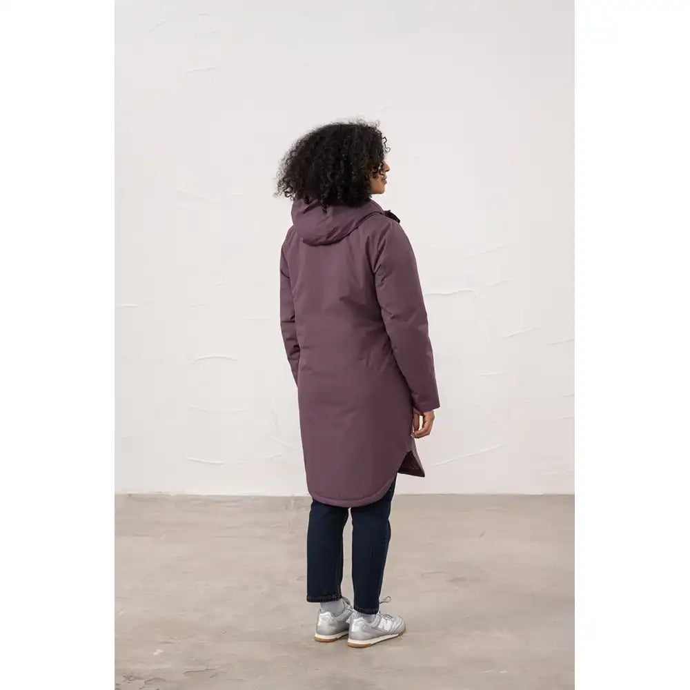 Person wearing a long purple coat standing against a white wall.