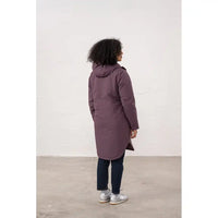 Person wearing a long purple coat standing against a white wall.