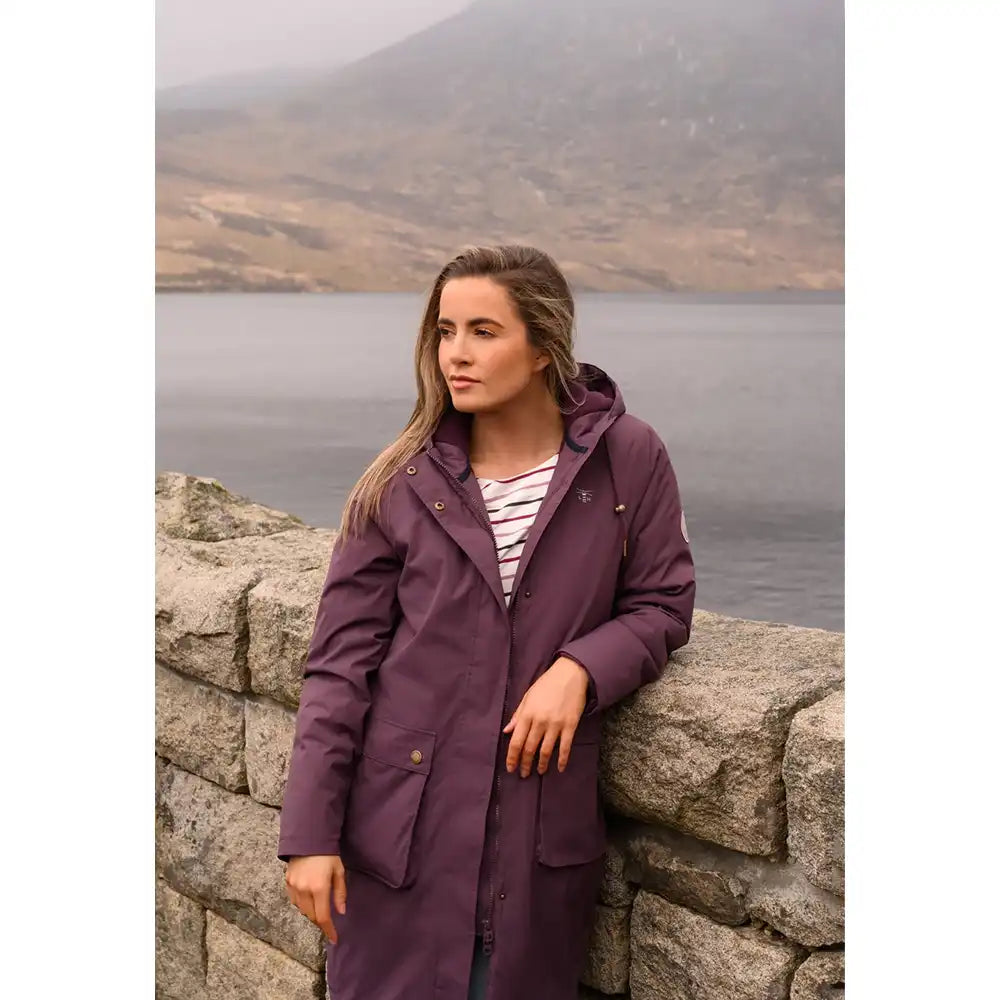 Woman in a purple coat standing by a lake with mountains in the background