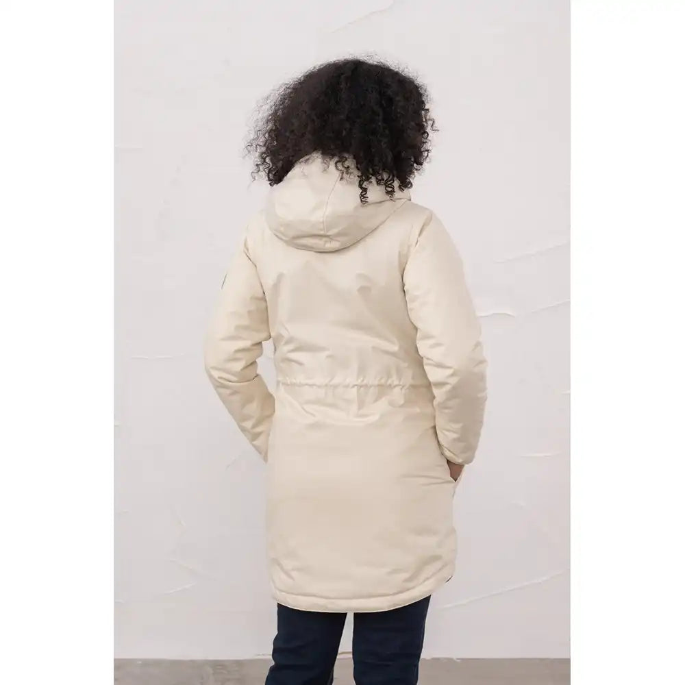 Person wearing a beige puffer coat against a white wall
