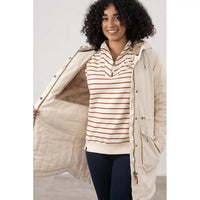 Woman wearing a beige jacket with a striped shirt and dark pants on a white background