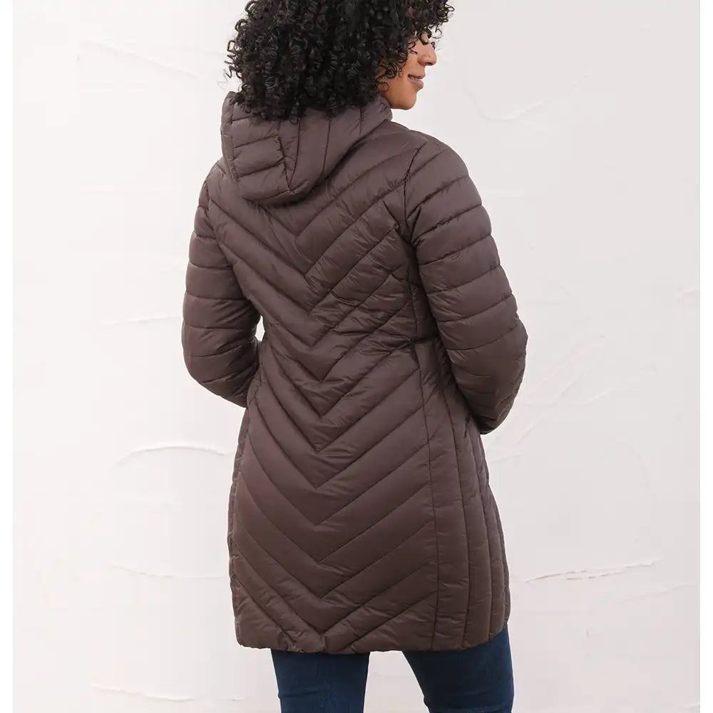 A woman shown from the back wearing a dark brown chevron-quilted hooded puffer coat, paired with dark blue jeans, against a white textured wall.