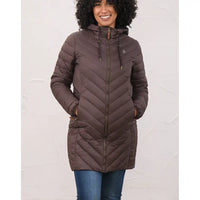 A woman wearing a brown hooded quilted puffer jacket with a front zipper and drawstrings, paired with blue jeans, standing against a light textured wall.