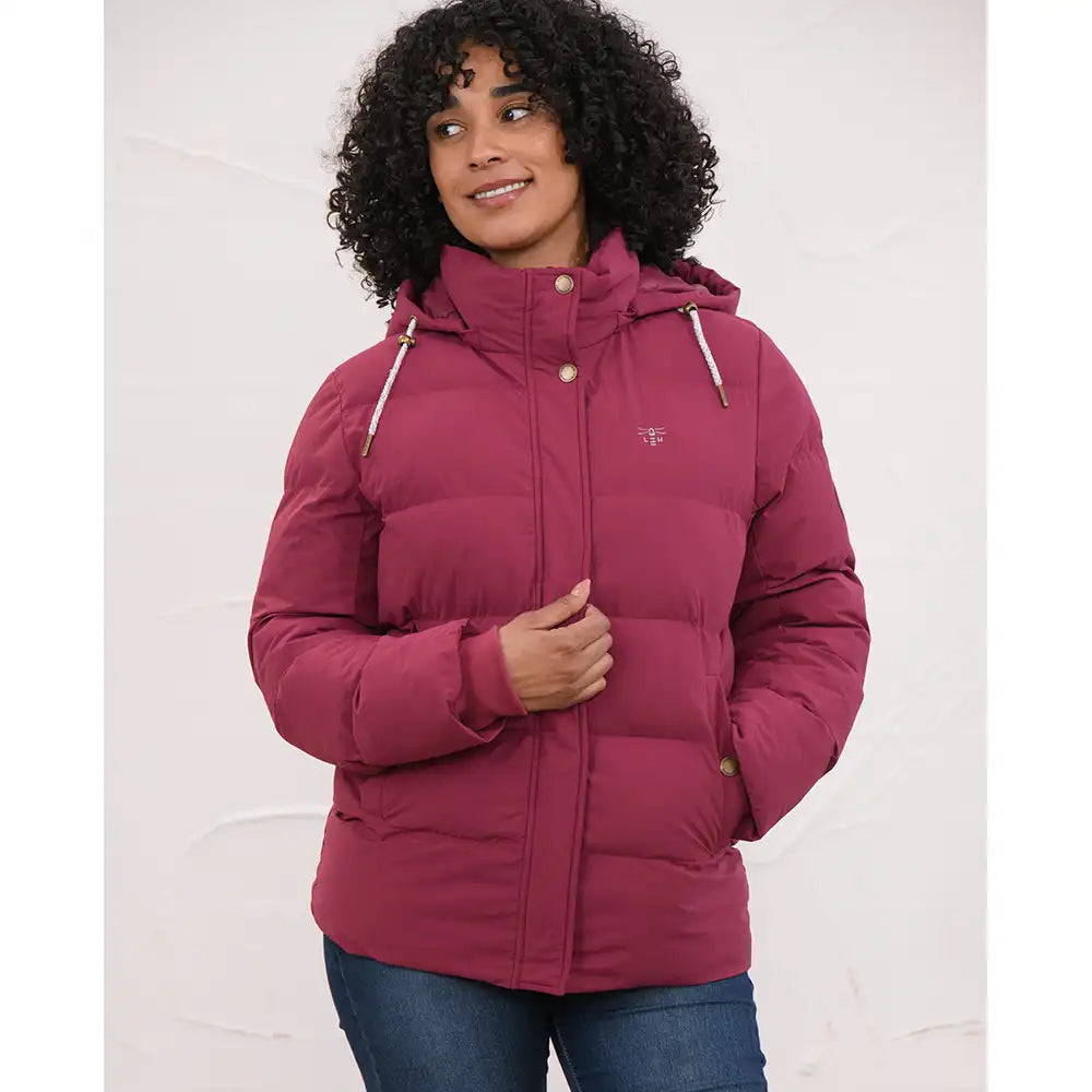 A woman wearing a dusty rose pink hooded puffer jacket with gold-tone buttons and a small embroidered logo on the left chest, paired with blue jeans, set against a plain white background.