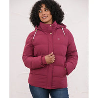 A woman wearing a dusty rose pink hooded puffer jacket with gold-tone buttons and a small embroidered logo on the left chest, paired with blue jeans, set against a plain white background.