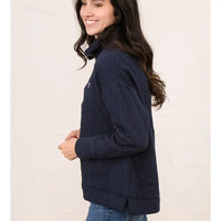A woman wearing a navy blue quilted jacket, shown from a side-back angle against a light beige textured wall.
