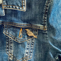 Close-up of a blue denim jacket with a blackbird pin on the chest pocket.