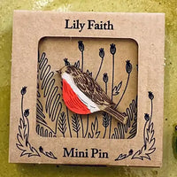 A wooden bird mini pin with a red breast, brown and white patterned wings, and a small yellow beak, displayed inside a square kraft paper window box labeled 'Lily Faith' and 'Mini Pin'.