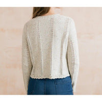 Person wearing a beige knitted cardigan with a pink background