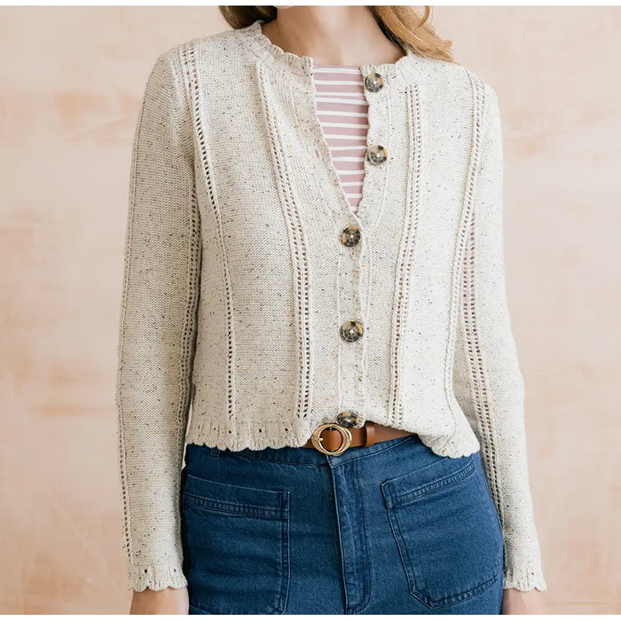 Person wearing a beige knitted cardigan over a striped shirt with a pink background