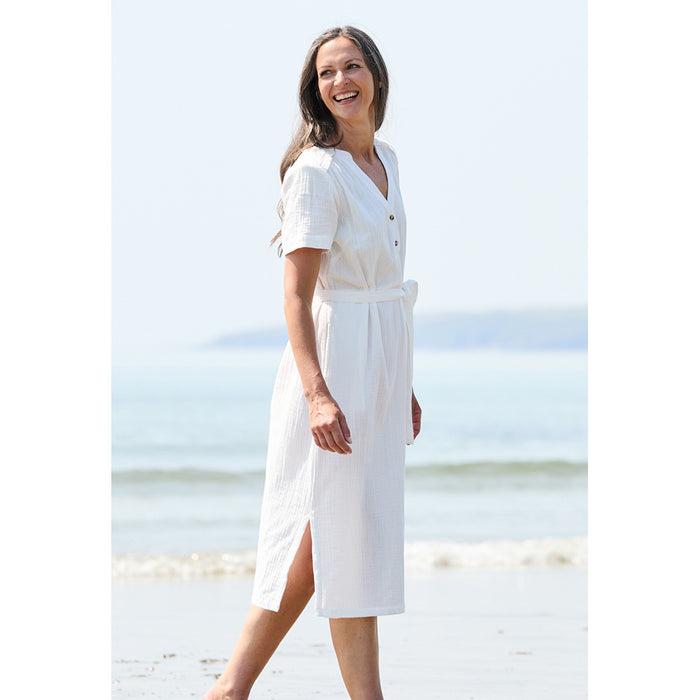 A women wearing a white dress from the side showing a side vent with a tie belt at the waist and short sleeves 