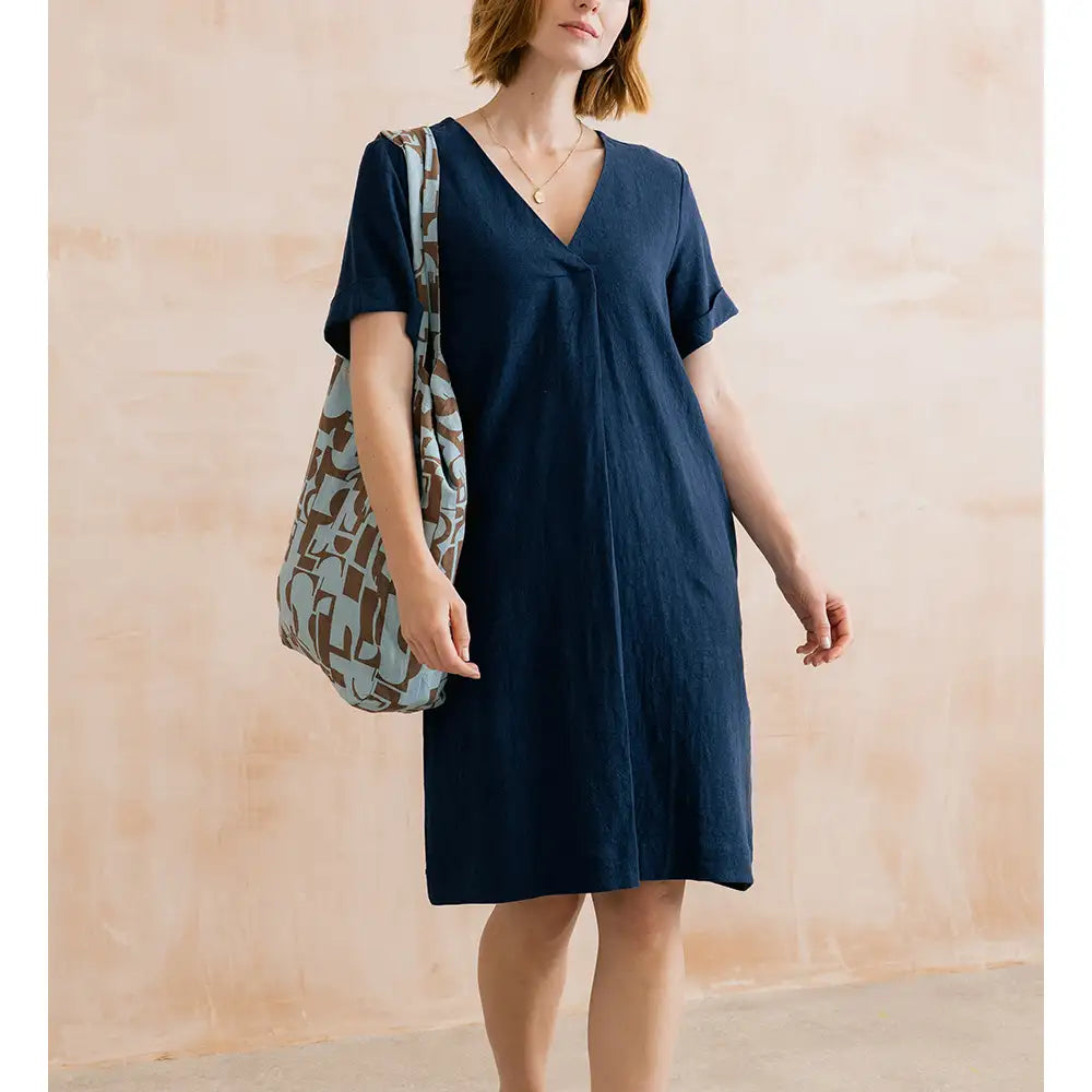 Woman wearing a navy blue dress holding a patterned bag against a beige wall.