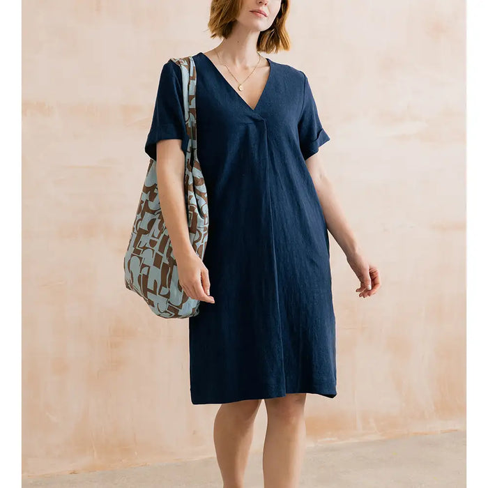Woman wearing a navy blue dress holding a patterned bag against a beige wall.