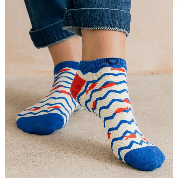 Person wearing blue jeans and patterned socks with red and blue designs on a beige floor.