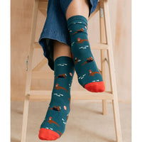 Person wearing teal socks with red toes and soles, sitting on a wooden stool.